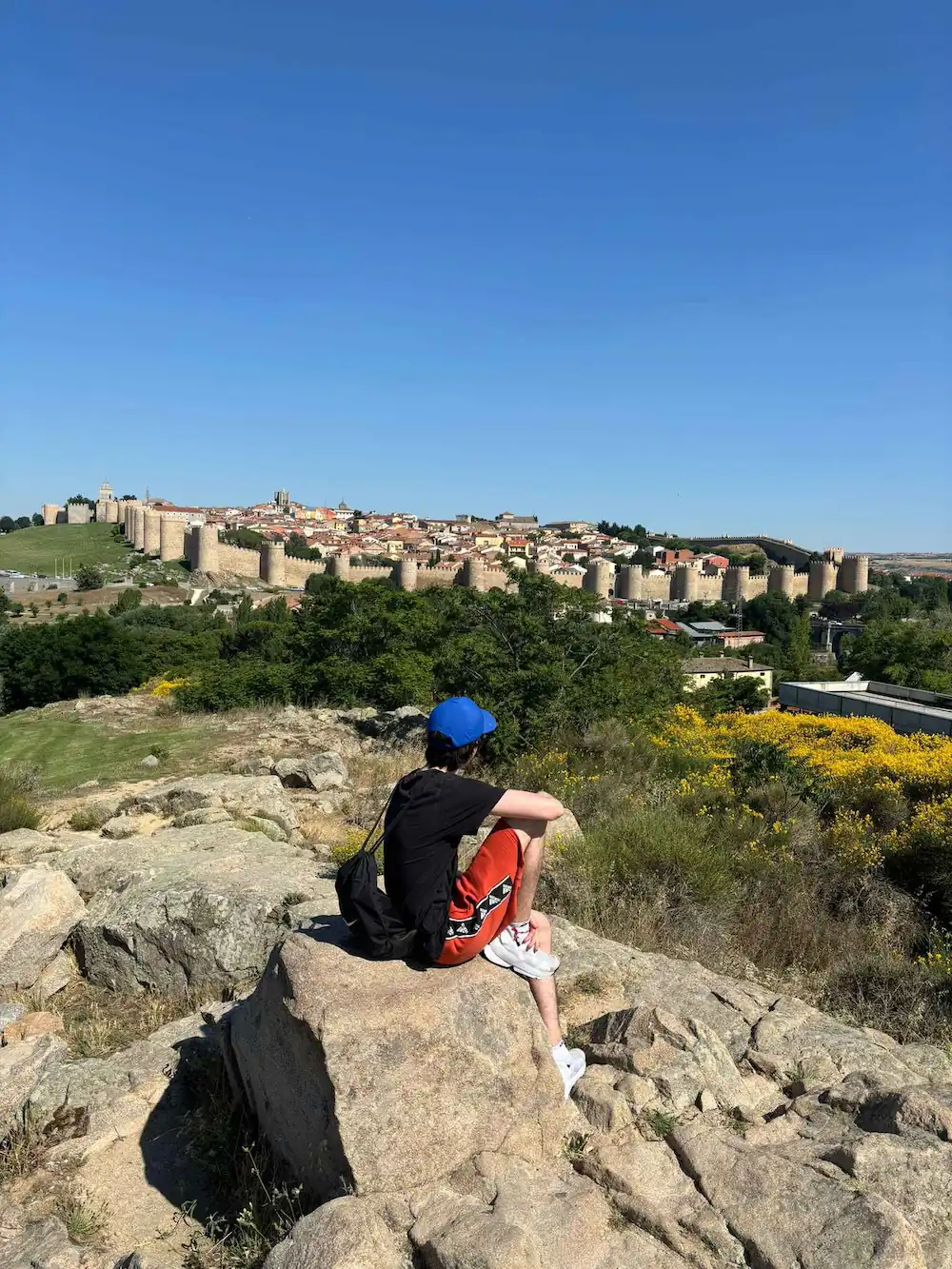 Joven sentado en una roca con vista a la ciudad.